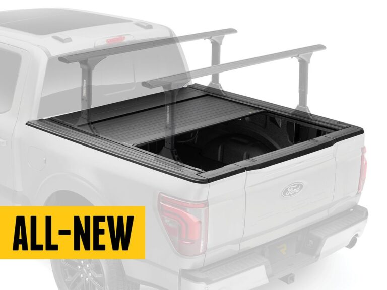 RealTruck FlushFit TS cover partially open on a silver Ford F-150 with T-slot rack mounted on top and ALL-NEW yellow text banner overlay, rear three-quarter angle