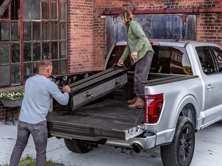 A man and woman removing the RetraxPRO EZ-OFF cover from a silver Ford F-150 in a brick-courtyard lifestyle setting, demonstrating easy two-person removal