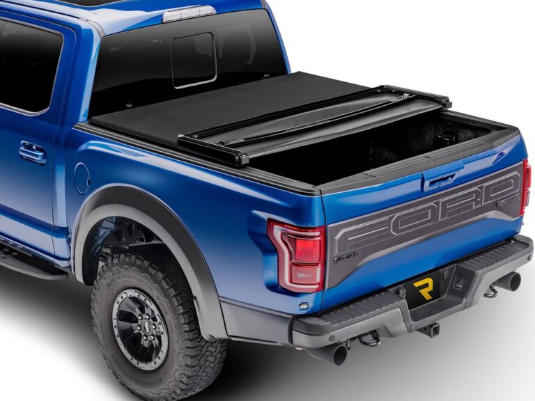 Extang Trifecta Signature 2.0 soft folding tonneau cover partially folded open with rear panels flipped up on a blue Ford F-150 Raptor, exposing the carpet-lined bed, rear three-quarter angle