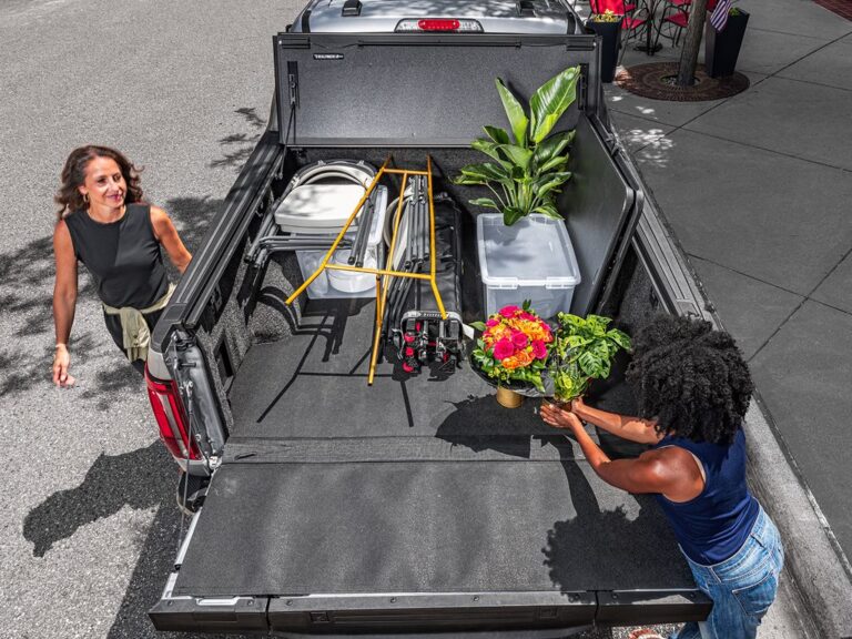 BAKFlip MX4 cover fully open and folded against the cab on a silver Ford F-150, two women loading plants and flowers into the bed, rear view