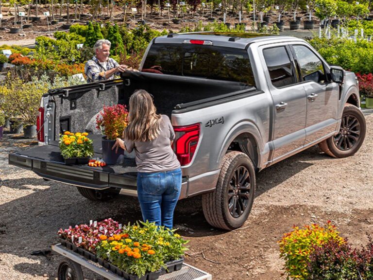 TruXedo TruXport GEN 2 lifestyle shot of a silver Ford F-150 with the cover partially open and dog crate in the bed, in a parking lot