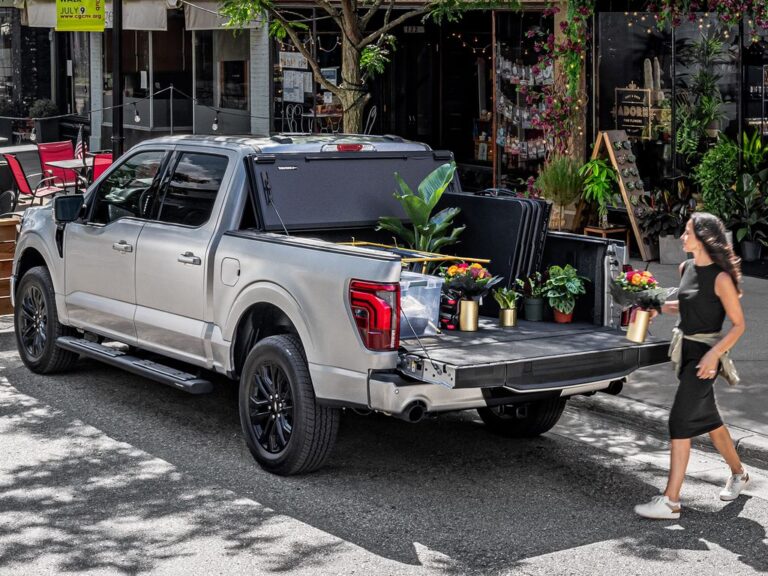 BAKFlip MX4 lifestyle shot on a silver Ford F-150 with the cover open against the cab, woman loading a flower bouquet into the bed, urban street setting