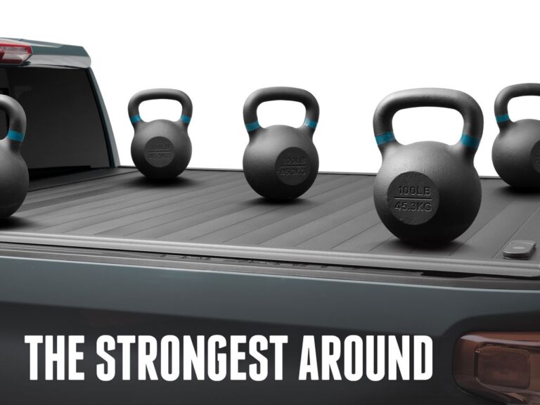 RetraxPRO MX cover with four 100-pound kettlebells resting on top to demonstrate 500-pound load rating, dark green truck rear view with THE STRONGEST AROUND marketing overlay