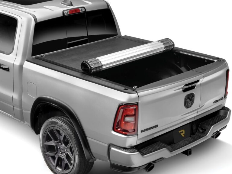 RealTruck BAK Revolver X2 hard roll-up tonneau cover partially rolled on a silver Ram 2500 Bighorn, rear three-quarter angle on white background