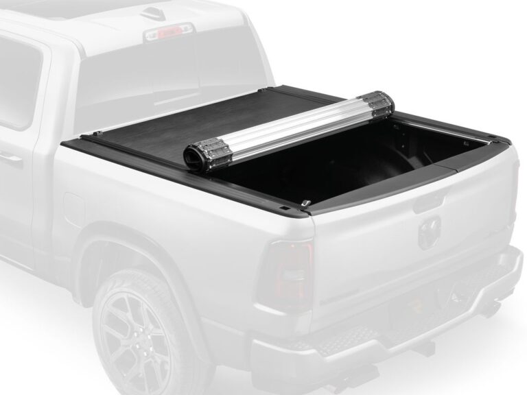 RealTruck BAK Revolver X2 hero marketing image with the cover partially rolled and a ghosted dimmed silver Ram truck in the background