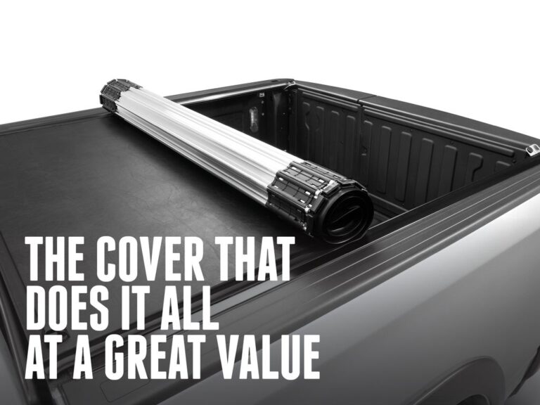 RealTruck BAK Revolver X2 hard roll-up cover with the cover panel unrolled and laid flat on a truck bed, white seamless studio background with marketing text overlay