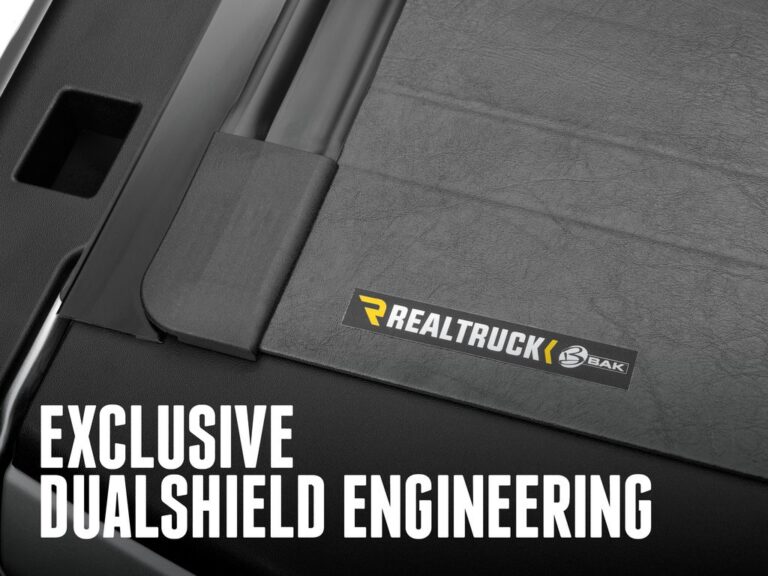 RealTruck BAK Revolver X2 close-up of the RealTruck x BAK branding badge on the cover material showing the DualShield vinyl texture, EXCLUSIVE DUALSHIELD ENGINEERING text