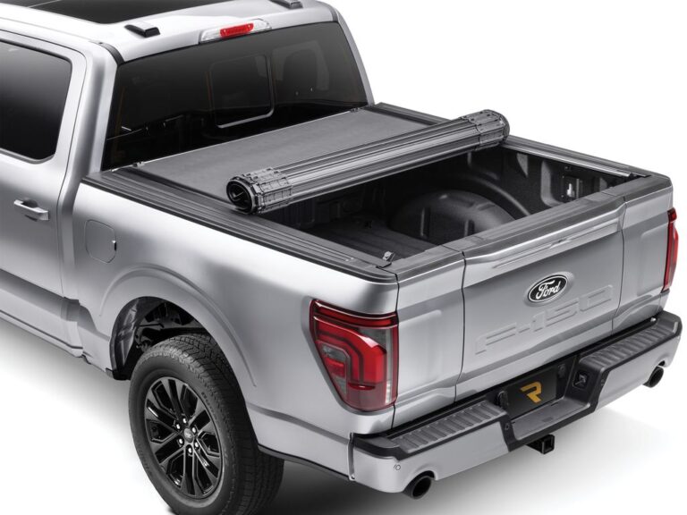 BAK Revolver X4S hard roll-up tonneau cover partially open on a silver Ford F-150, right rear three-quarter view showing the rolled cover bundle at the bulkhead, RealTruck product shot on white background