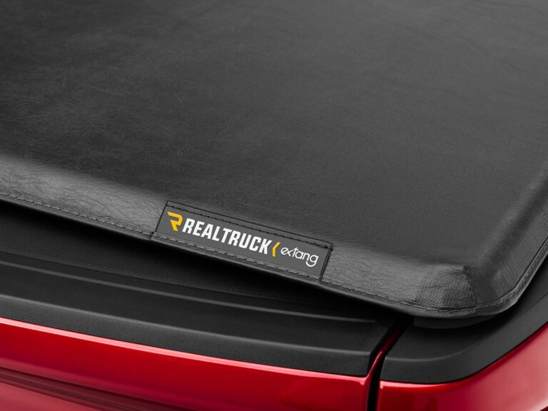 Close-up of the Trifecta 2.0 corner with the RealTruck Extang badge and leather-grain vinyl showing the corner-tuck system on a red truck
