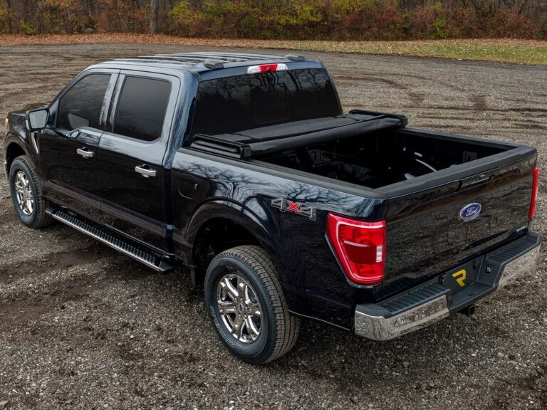 Black Ford F-150 4x4 with Trifecta 2.0 cover partially folded forward against the cab, two-thirds bed access, autumn outdoor setting