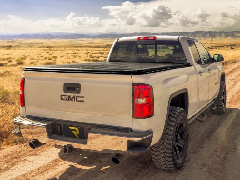 White GMC Sierra 4x4 with Trifecta 2.0 cover closed, rear three-quarter angle showing the GMC tailgate badge, desert landscape lifestyle shot