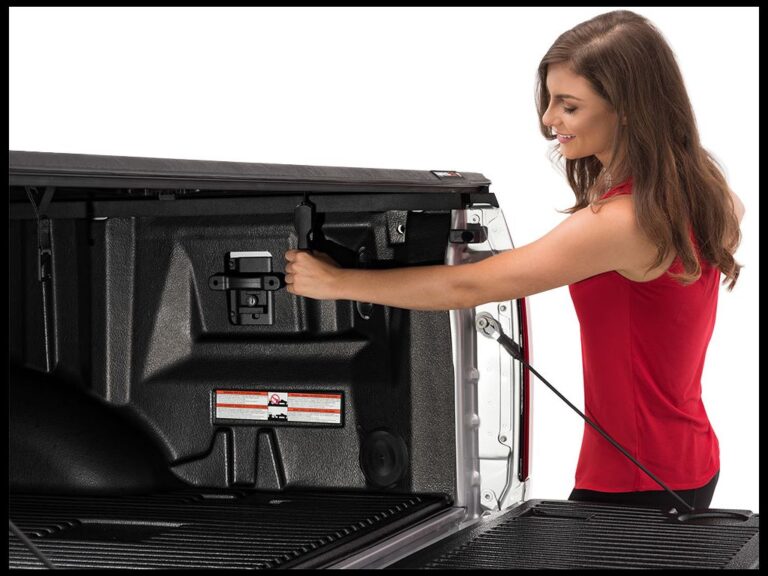 Studio shot of a woman in red shirt opening the tailgate of a silver truck, revealing the closed Trifecta 2.0 cover folded forward against the cab